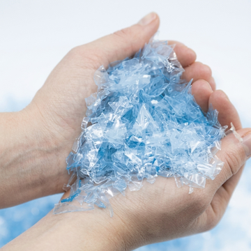 Hands holding shredded blue recycled ocean plastic flakes.