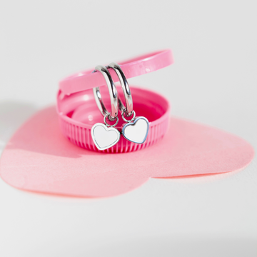 Silver hoop earrings with white heart charms resting on a pink heart-shaped base.